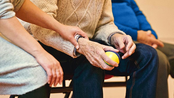 A PSW helping a man do hand exercises with a soft ball.