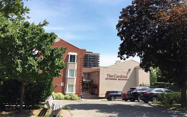 Photo of the Cardinal Retirement Residence on a sunny day in the afternoon. There are two huge trees in the front.